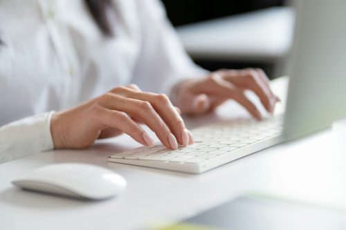 Close-Up Of Woman Typing On White Computer Keyboard In Office